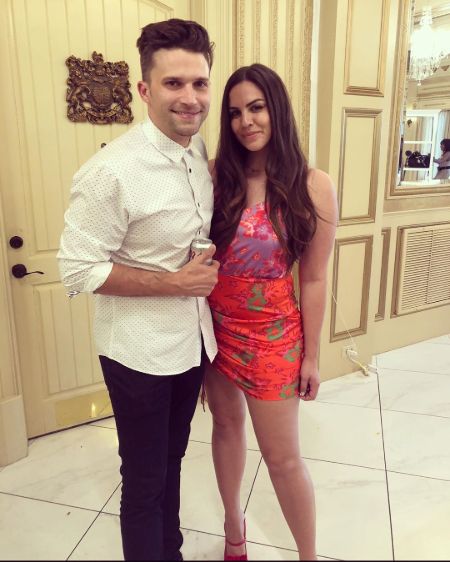 Katie Maloney in a orange dress poses a picture with husband Tom Schwartz.